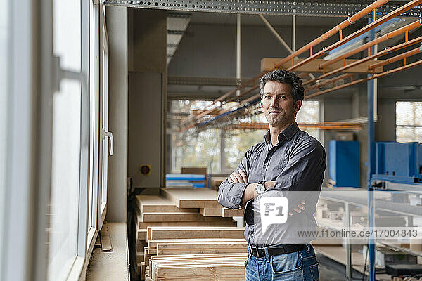 Portrait of carpenter posing in production hall with crossed arms