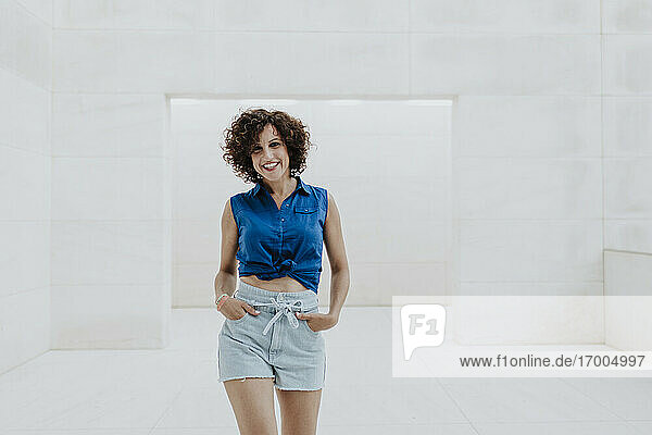 Cheerful woman with curly hair standing on floor against tiled wall