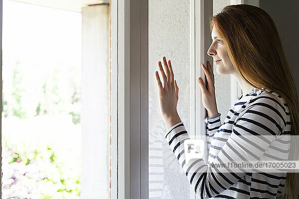 Frau schaut durch ein Fenster  während sie zu Hause steht