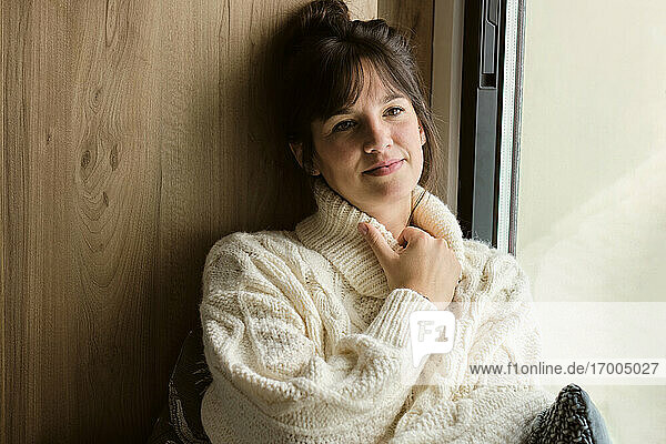 Thoughtful woman in sweater sitting by window at home
