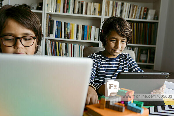 Lächelnder Junge mit digitalem Tablet,  der mit einem männlichen Freund zu Hause sitzt