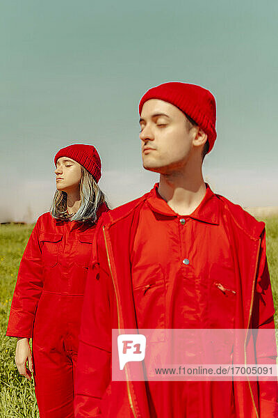 Young couple wearing red overalls and hats standing in nature with eyes closed