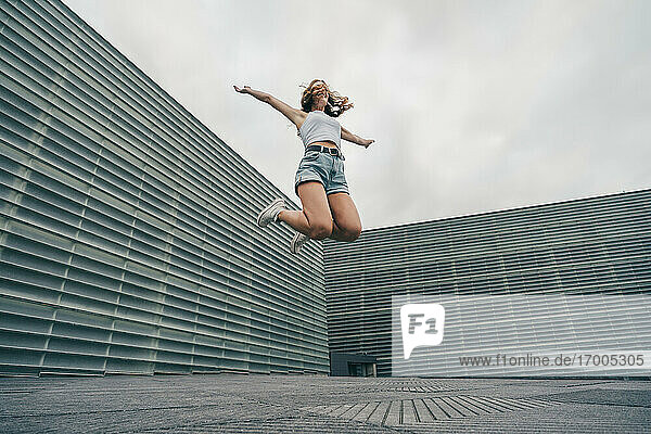 Carefree woman with arms outstretched jumping against wall