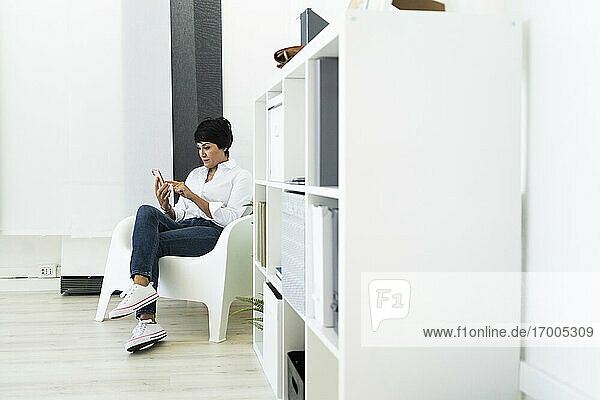 Businesswoman sitting in office armchair with smart phone in hands