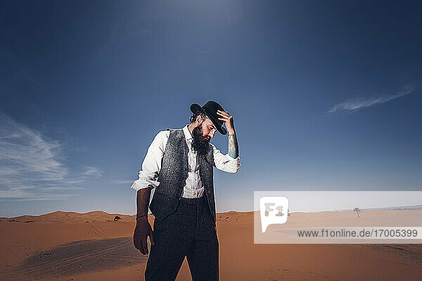 Man with a beard and hat in the dunes of the desert of Morocco