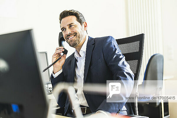 Smiling businessman talking on telephone while sitting on chair at office