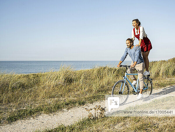 Junge Frau genießt die Fahrt mit einem Mann auf dem Fahrrad gegen den klaren Himmel