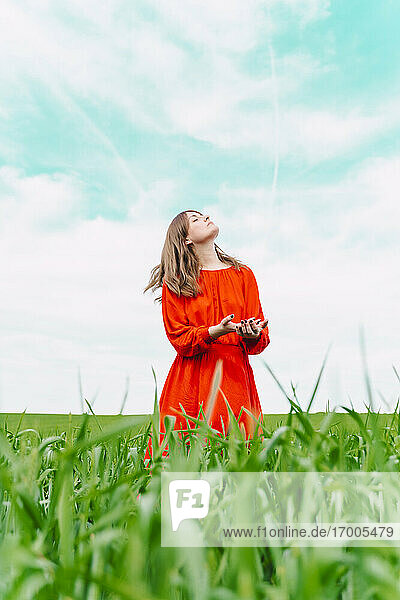 Frau in rotem Kleid steht auf einem Feld und schaut nach oben