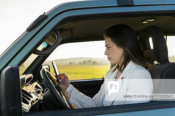 Young woman using mobile phone while sitting in car during road trip