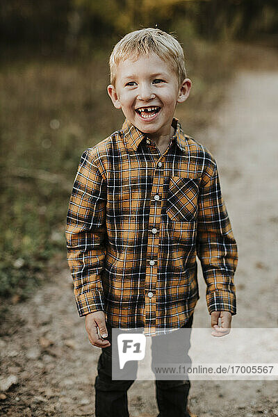 Lächelnder Junge mit kariertem Hemd auf einem Fußweg im Wald