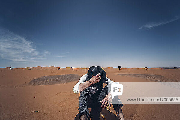 Mann  der seinen Hut in den Dünen der Wüste von Marokko aufsetzt