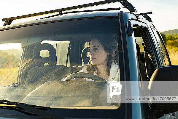 Nachdenkliche junge Frau hinter der Windschutzscheibe  die wegschaut  während sie während einer Autofahrt im Auto sitzt