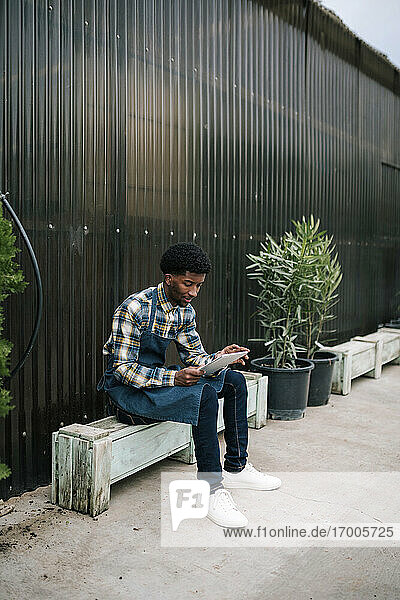 Male worker using digital tablet while sitting on bench against corrugated iron wall