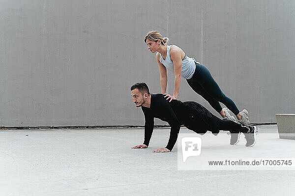 Young sportsman doing push-ups with woman on his back against wall