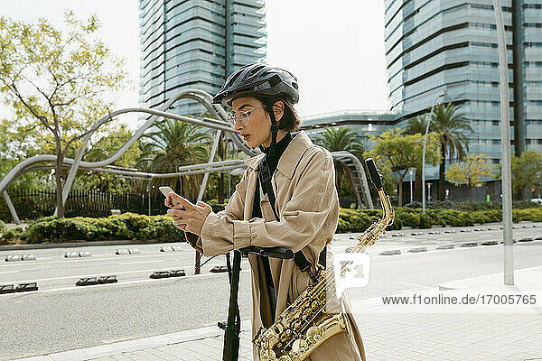 Frau mit Saxophon  die ein Mobiltelefon benutzt  während sie auf einem Motorroller in der Stadt steht