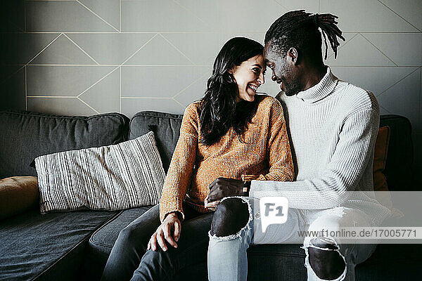 Romantischer Mann und schwangere Frau sehen sich gegenseitig an  während sie zu Hause auf dem Sofa sitzen