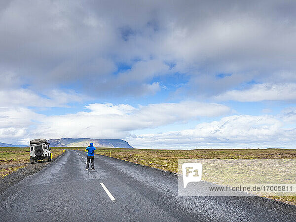 Man standing in middle of remote asphalt road  Iceland