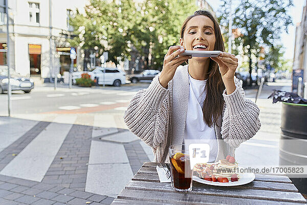 Frau  die ein Foto von Essen und Getränken auf dem Tisch macht  während sie in einem Café auf dem Bürgersteig sitzt