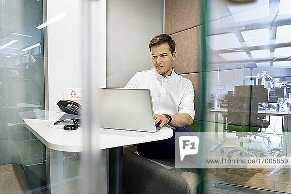 Junger Geschäftsmann arbeitet am Laptop  während er am Schreibtisch im Büro sitzt