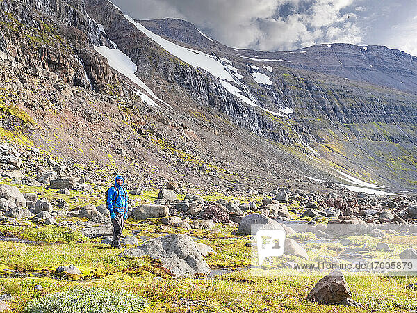 Männlicher Wanderer inmitten von Felsbrocken in einem isländischen Tal