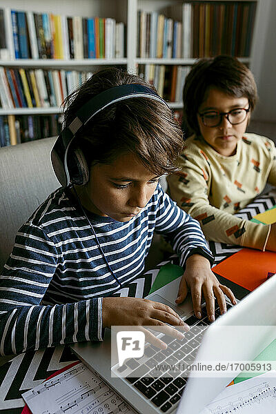 Junge mit Laptop beim E-Learning mit einem männlichen Freund zu Hause sitzend