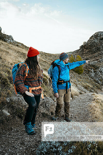 Mittlerer erwachsener Mann  der beim Wandern mit seiner Freundin auf einem felsigen Berg im Urlaub auf etwas zeigt