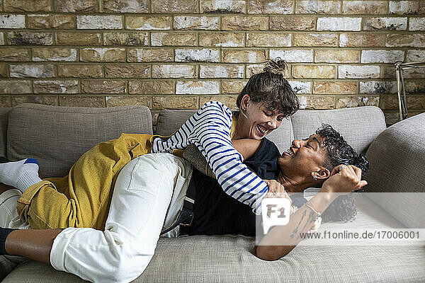Playful woman leaning on girlfriend lying on sofa at home