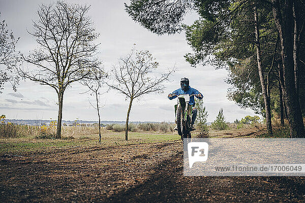 Teenage male rider performing wheelie on dirt road in forest