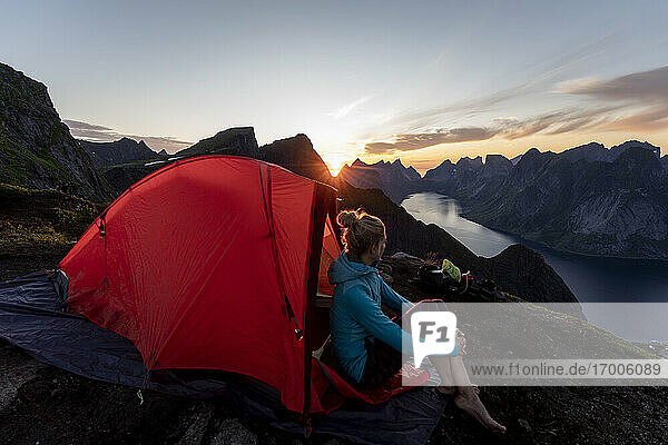 Frau bewundert die Aussicht  während sie im Lager auf dem Berg Reinebringen sitzt. Lofoten  Norwegen
