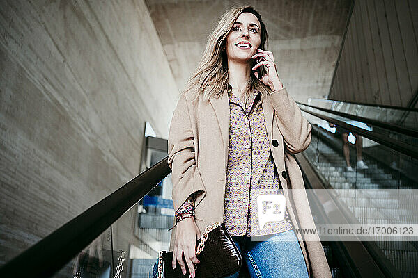 Schöne Frau  die mit ihrem Mobiltelefon spricht  während sie auf einer Rolltreppe nach unten fährt