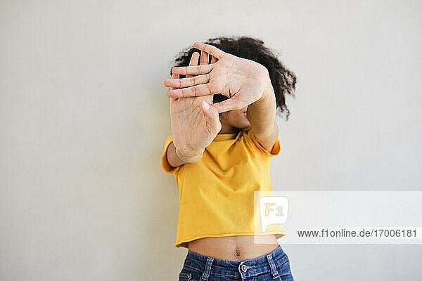 Frau zeigt Stop-Geste  während sie gegen eine weiße Wand steht
