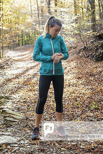 Sportswoman checking time while standing on forest path