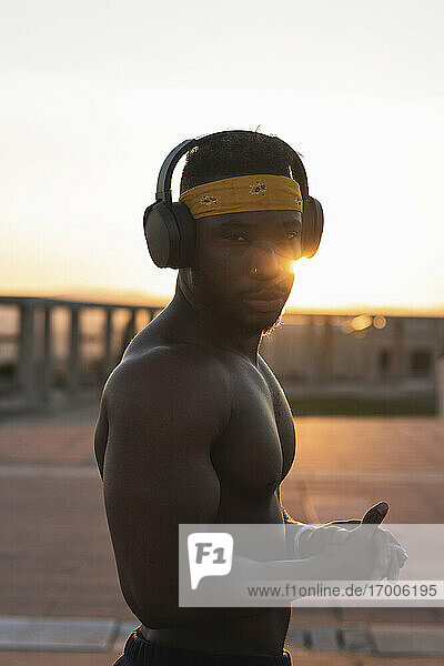 Sportler trägt Kopfhörer und hört Musik  während er bei Sonnenuntergang im Park steht