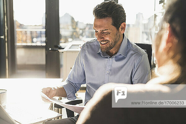 Smiling businessman analyzing document while working with colleague at office