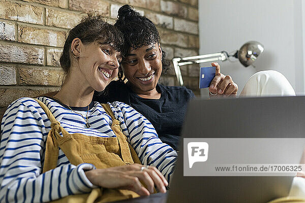 Lesbisches Paar  das beim Online-Shopping auf dem Laptop zu Hause auf die Kreditkarte schaut