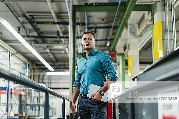 Confident male professional with digital tablet looking away in factory