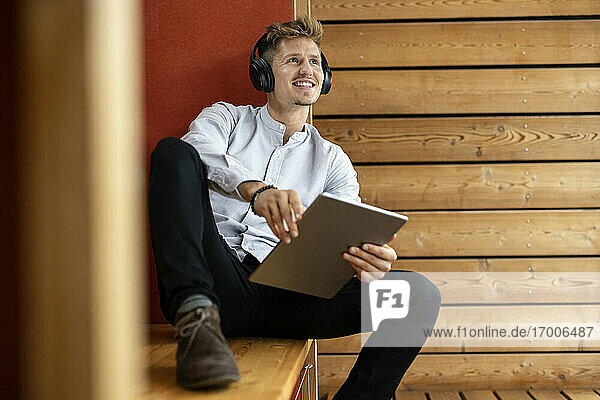 Mann mit Kopfhörern und digitalem Tablet  der wegschaut  während er zu Hause sitzt
