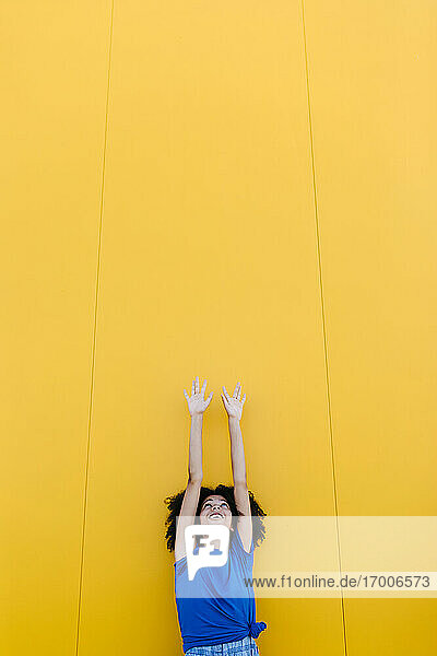 Lächelnde Frau  die nach oben zur gelben Wand greift
