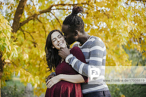 Afrikanischer Mann küsst glückliche schwangere Frau im Park im Herbst