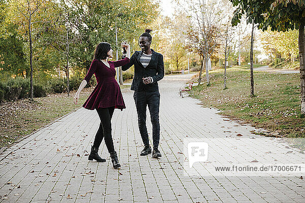 Glückliches multiethnisches Paar tanzt im Park im Herbst
