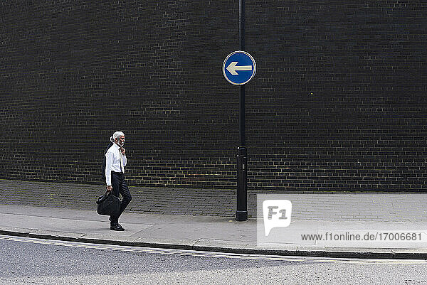 Eleganter älterer Geschäftsmann mit Gepäck  der auf dem Bürgersteig in die entgegengesetzte Richtung geht