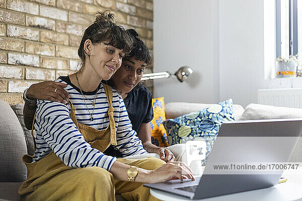 Lesbisches Paar benutzt einen Laptop  während es zu Hause auf dem Sofa sitzt