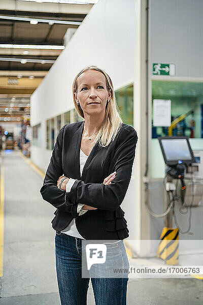 Confident blond female entrepreneur with arms crossed standing in industry