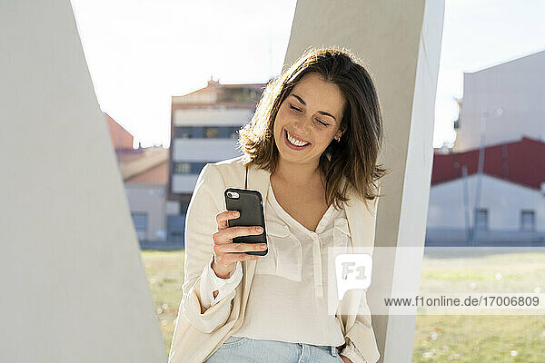Lächelnde Geschäftsfrau mit Smartphone in der Stadt an einem sonnigen Tag
