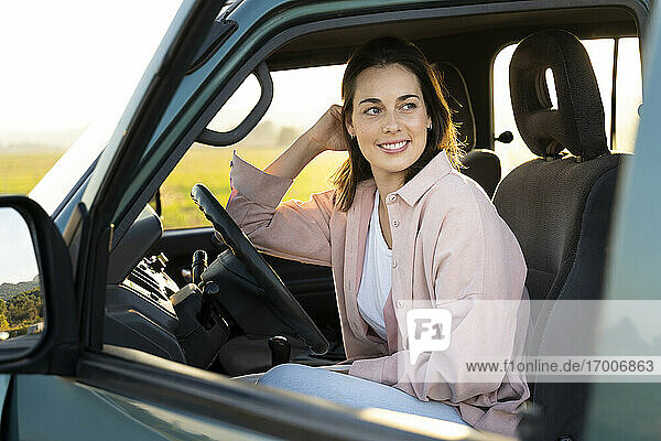 Lächelnde junge Frau  die im Auto sitzend wegschaut  während einer Autoreise
