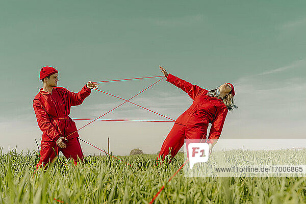 Young couple wearing red overalls and hats performing on a field with red string