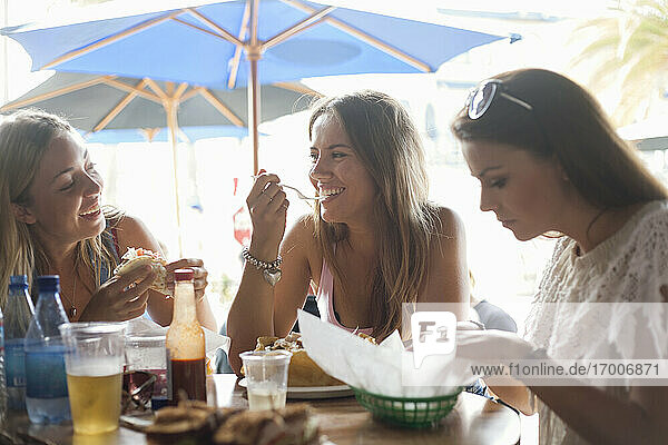 Happy female friends having lunch at beach restaurant during vacation