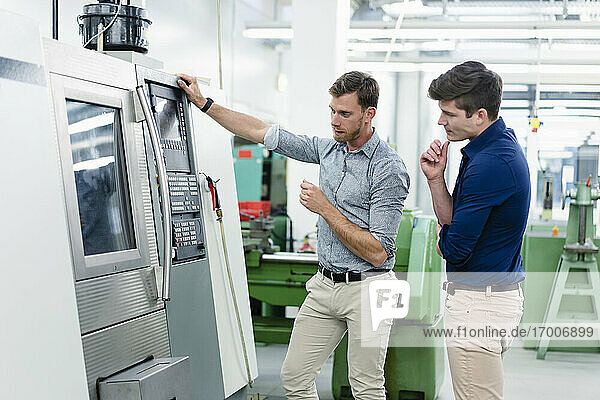 Male coworkers examining machinery equipment in industry