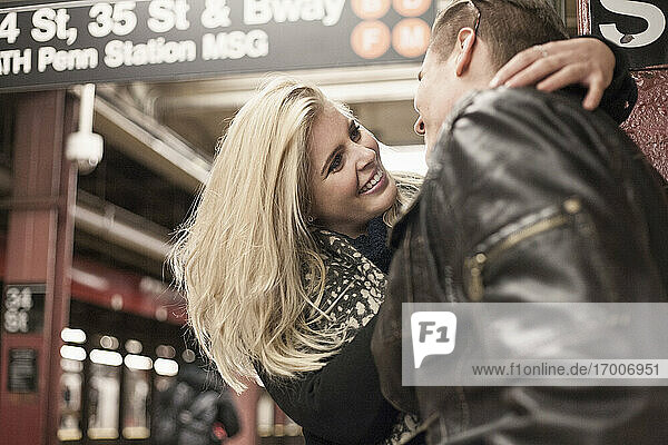 Lächelnde Frau  die einen Mann umarmt  während sie in einer U-Bahn-Station steht