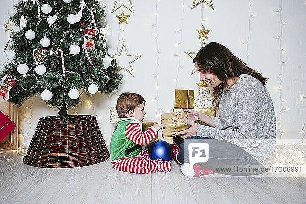 Eine Frau beschenkt einen kleinen Jungen  während sie an Weihnachten zu Hause sitzt